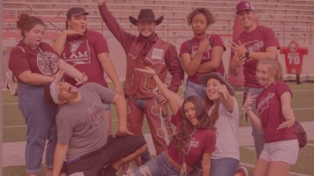 A red filtered image of several people on a football field wearing New Mexico State themed shirts and outfits.